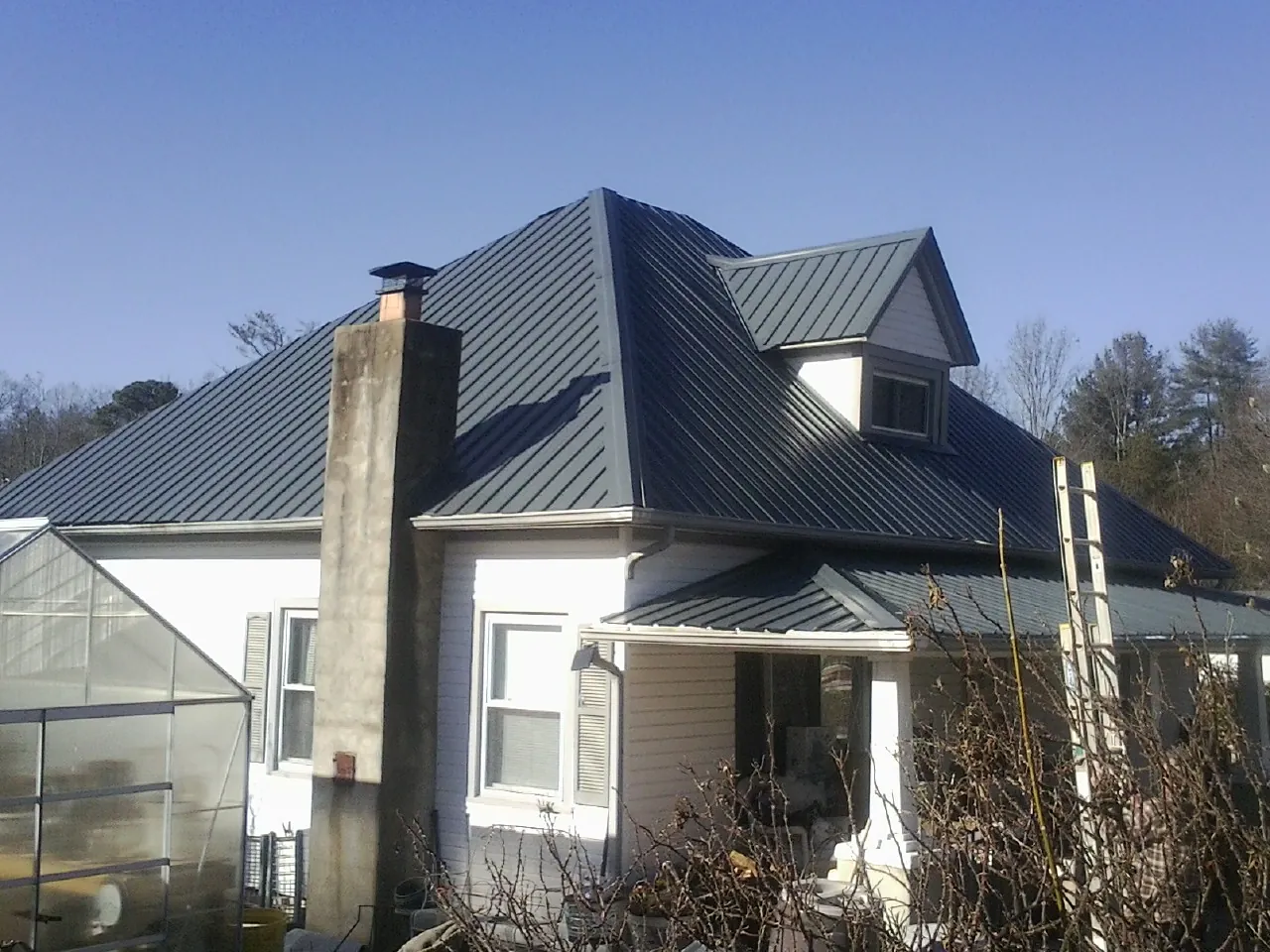Dark blue standing seam metal roof on a white farmhouse with dormer — Slate & Tile Roof Repair by Roofing Brothers in Great Neck