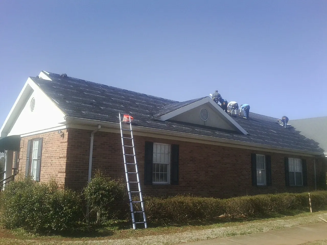 Crew tearing shingles off a brick ranch roof with a ladder set — Metal Roof Repair work by our crew in Great Neck