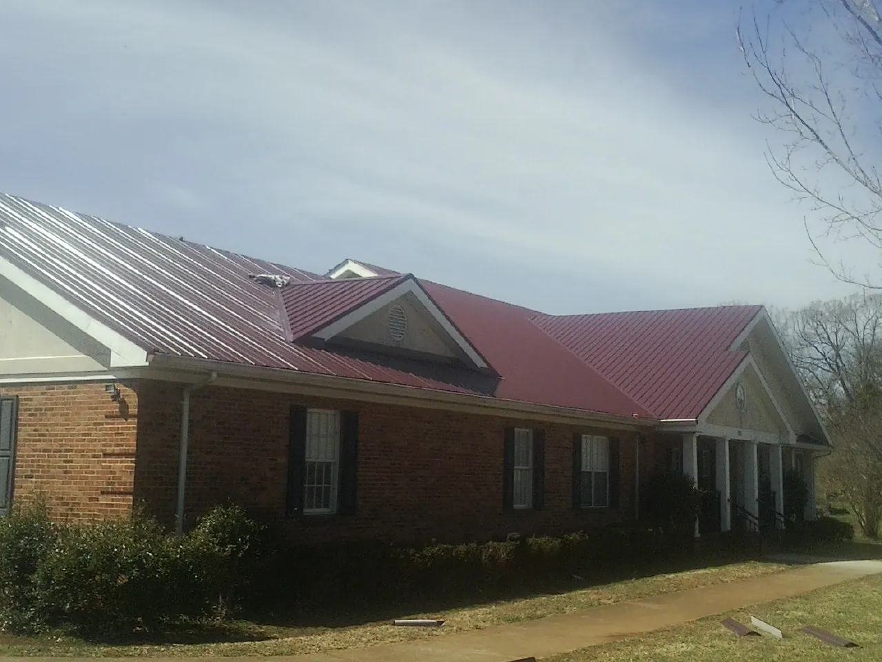 Red metal roof with gabled entries on a long brick building, from a Hail Damage Roof Repair job in Great Neck