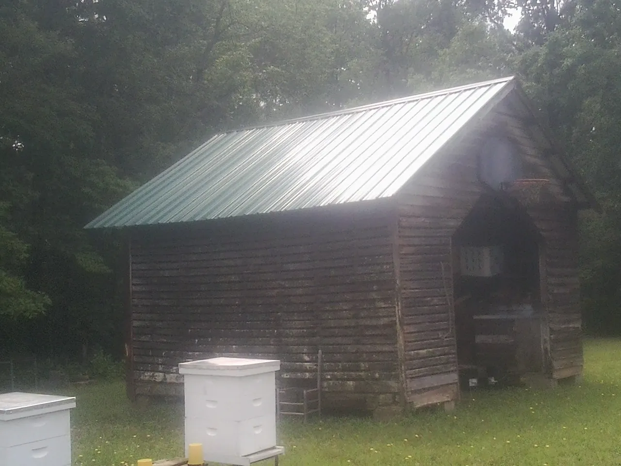 Green metal roof on a weathered barn beside stacked beehives in Great Neck