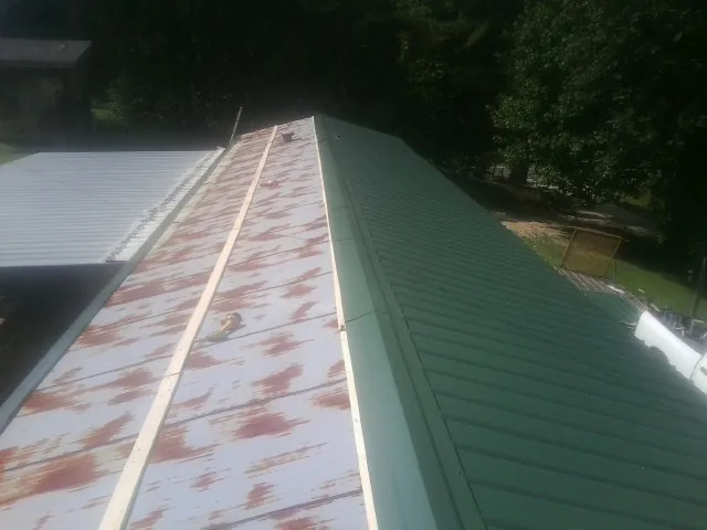 Old rusted panels beside newly installed green metal roofing — Wind Damage Roof Repair by Roofing Brothers in Great Neck
