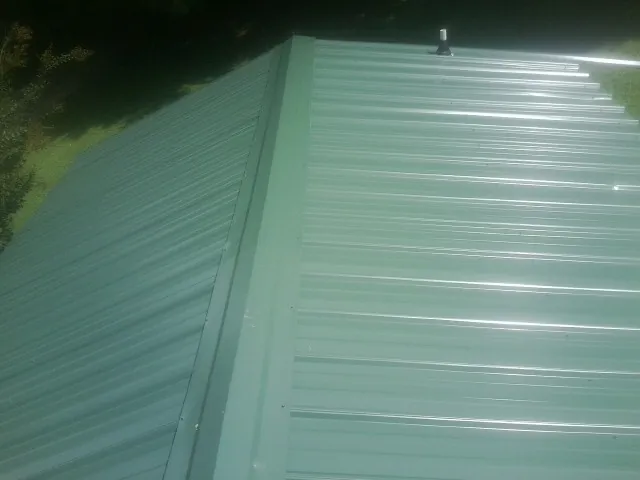 New green metal panels meeting at the ridge of a roof — Flat Roof Repair work by our crew in Great Neck