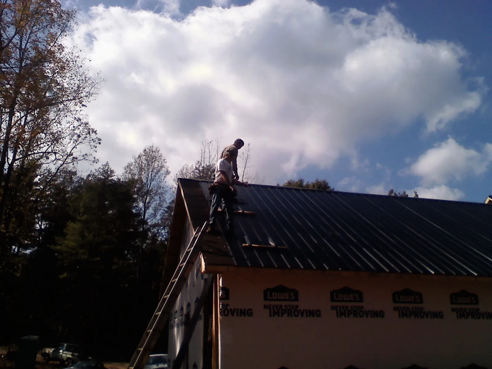 Roofer fastening dark metal panels high against a cloudy sky, from a Roof Inspection job in Great Neck
