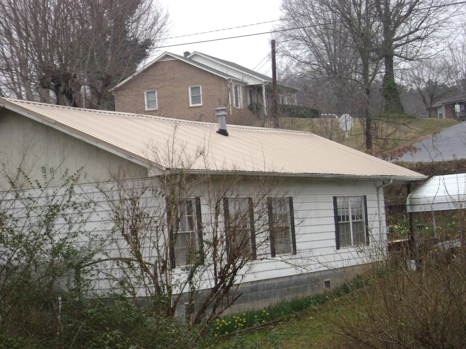 Tan metal roof on a white sided house set into a hillside — Commercial Roofing by Roofing Brothers in Great Neck