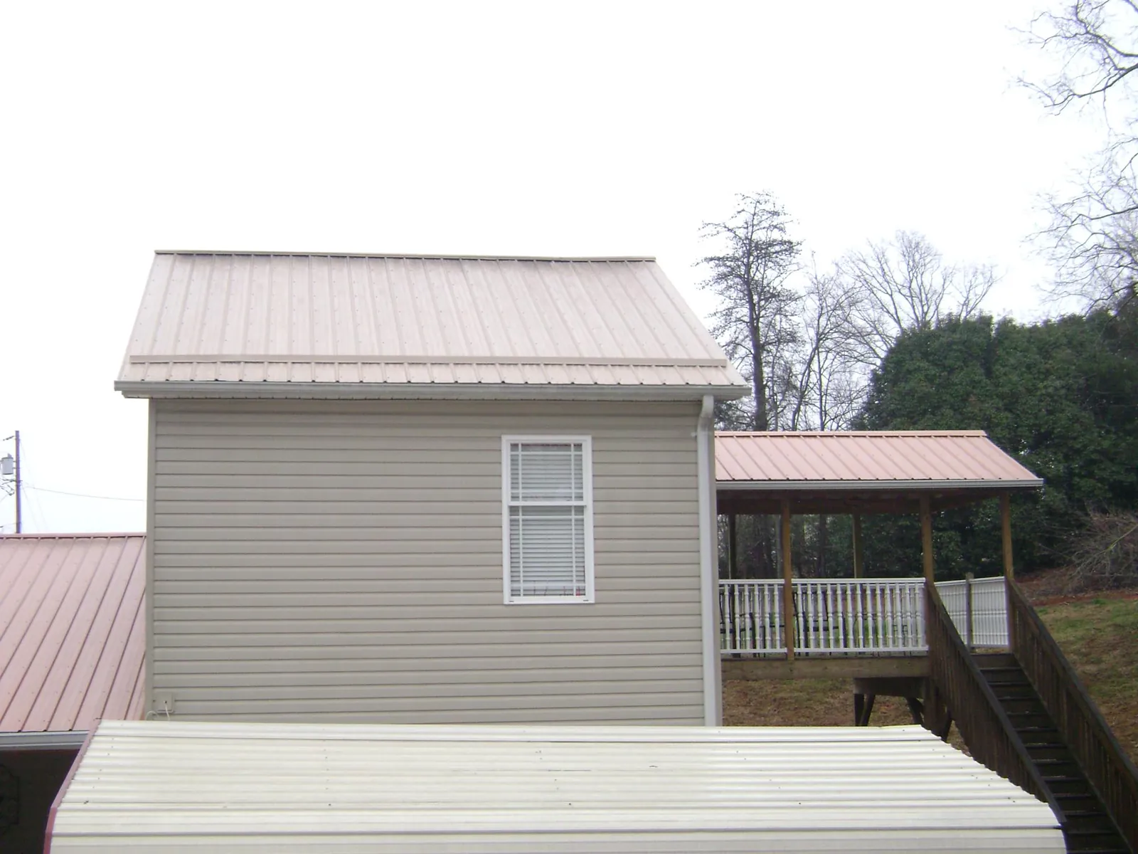 Tan metal roofs on a two story addition and attached porch, from a Roof Replacement job in Great Neck