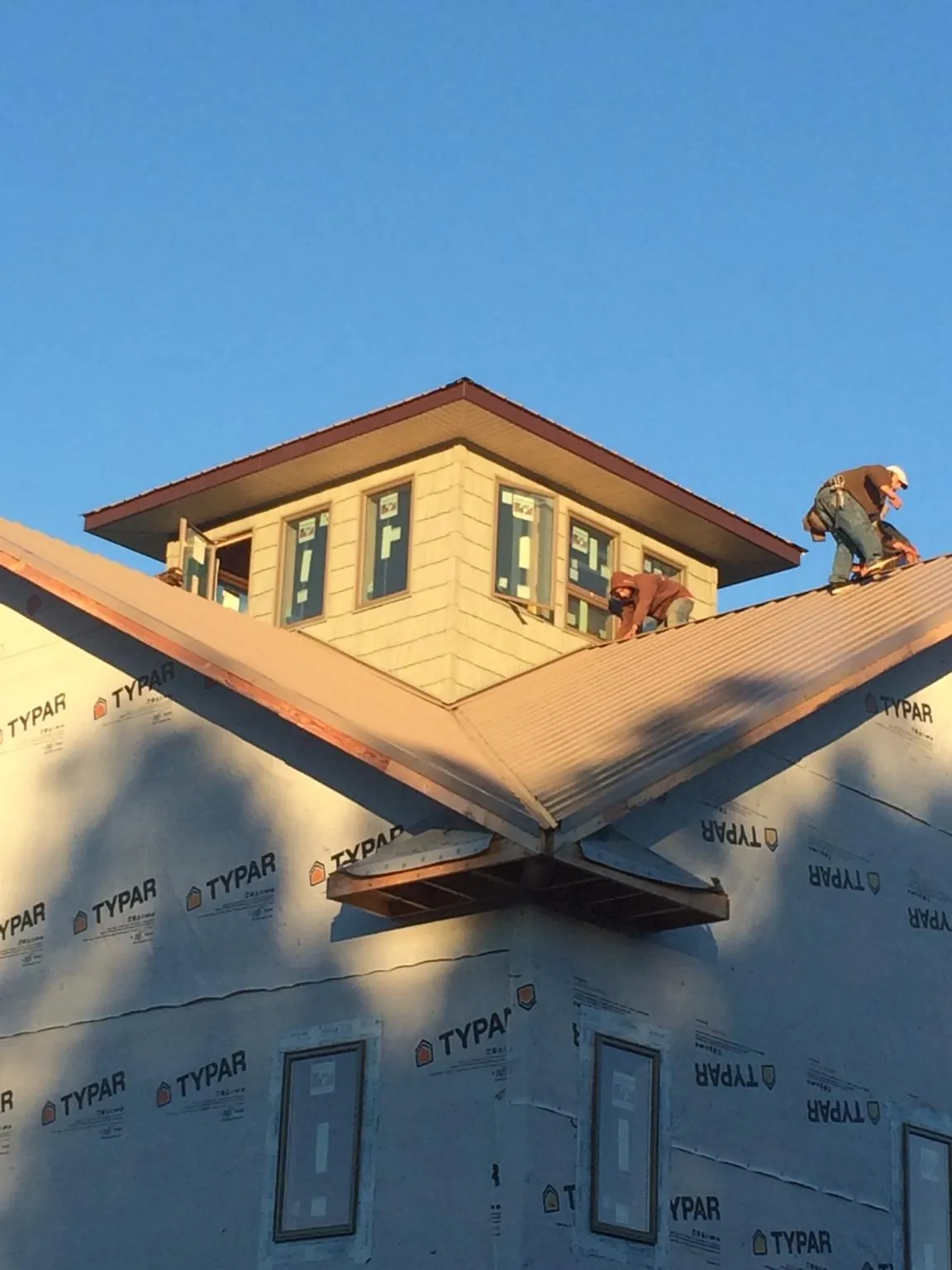 Roofers working around a rooftop cupola on a new metal roof at sunset — Roof Waterproofing in Great Neck by Roofing Brothers